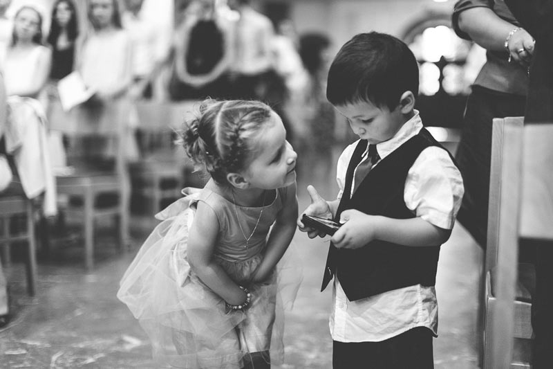 little girl looking at boy playing with his video game during wedding ceremony