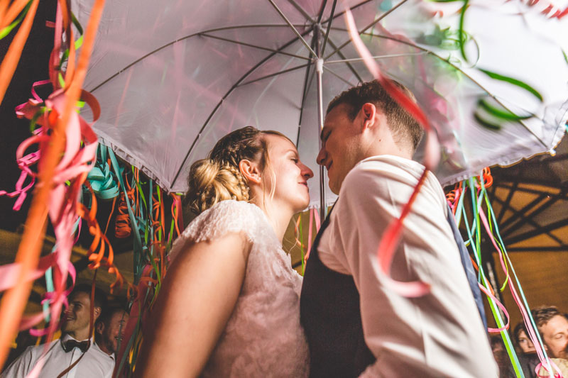 les mariés sous un parapluie de serpentins